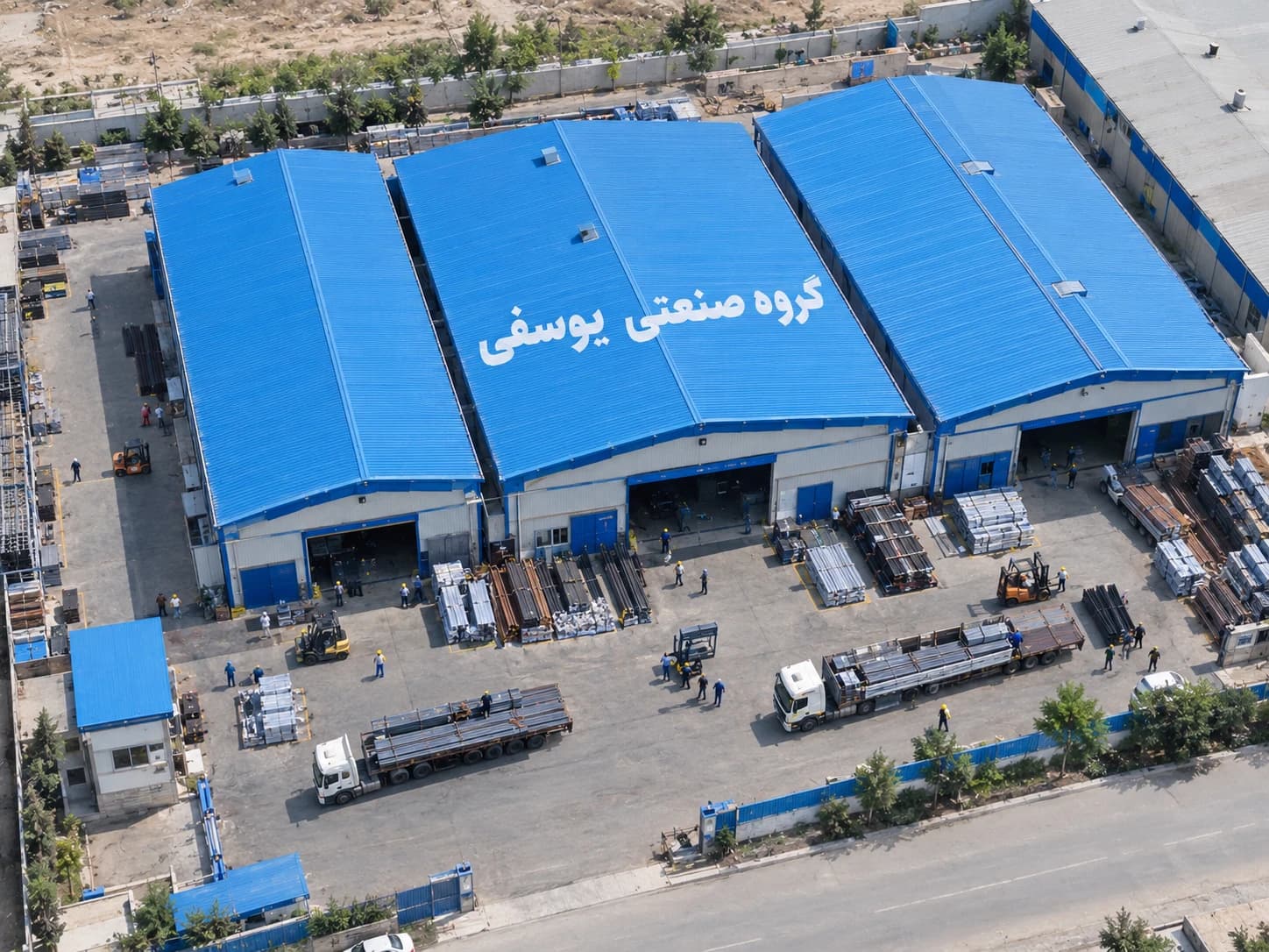 نمای هوایی کارخانه گروه صنعتی یوسفی با سوله‌های آبی، کامیون‌های حمل پروفیل و محوطه بارگیری